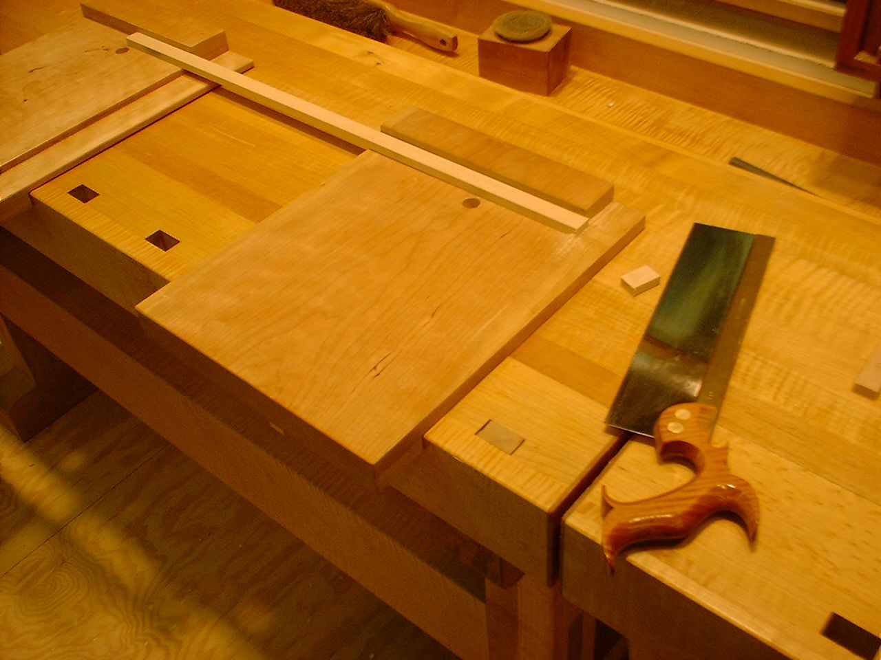 A bench hook on a workbench: a wide board with a batten along its far edge, a backsaw lying beside it