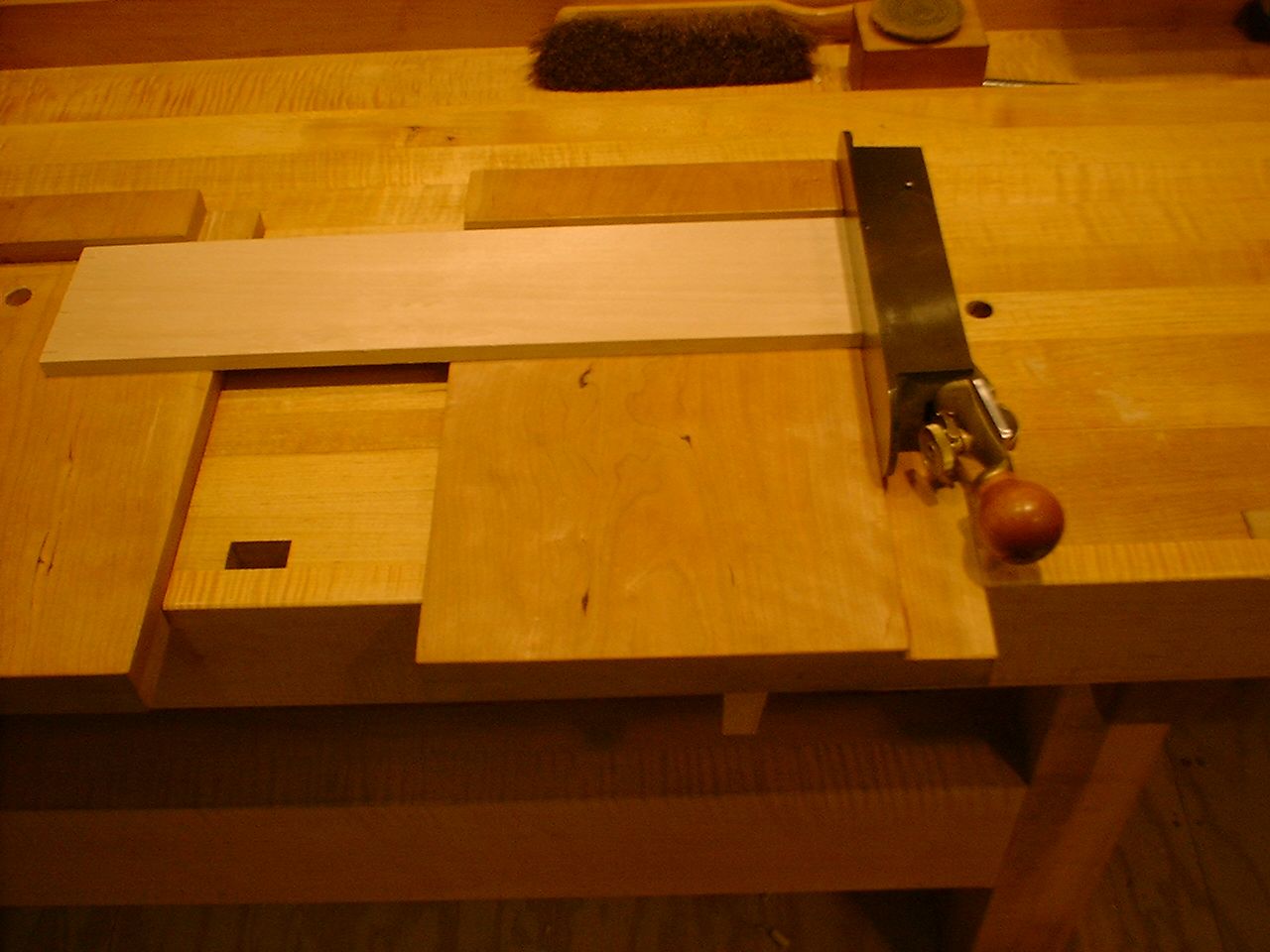 A shooting board on a workbench: a part lies on the platform against the stop, with a plane on its side at the end of it